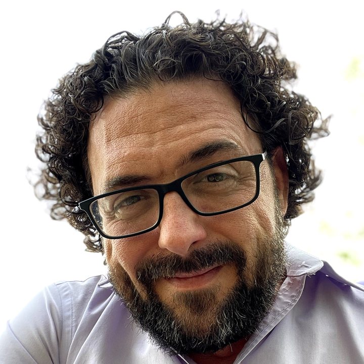 Justin Vitovsky, smiling, with curly hair, glasses and a beard